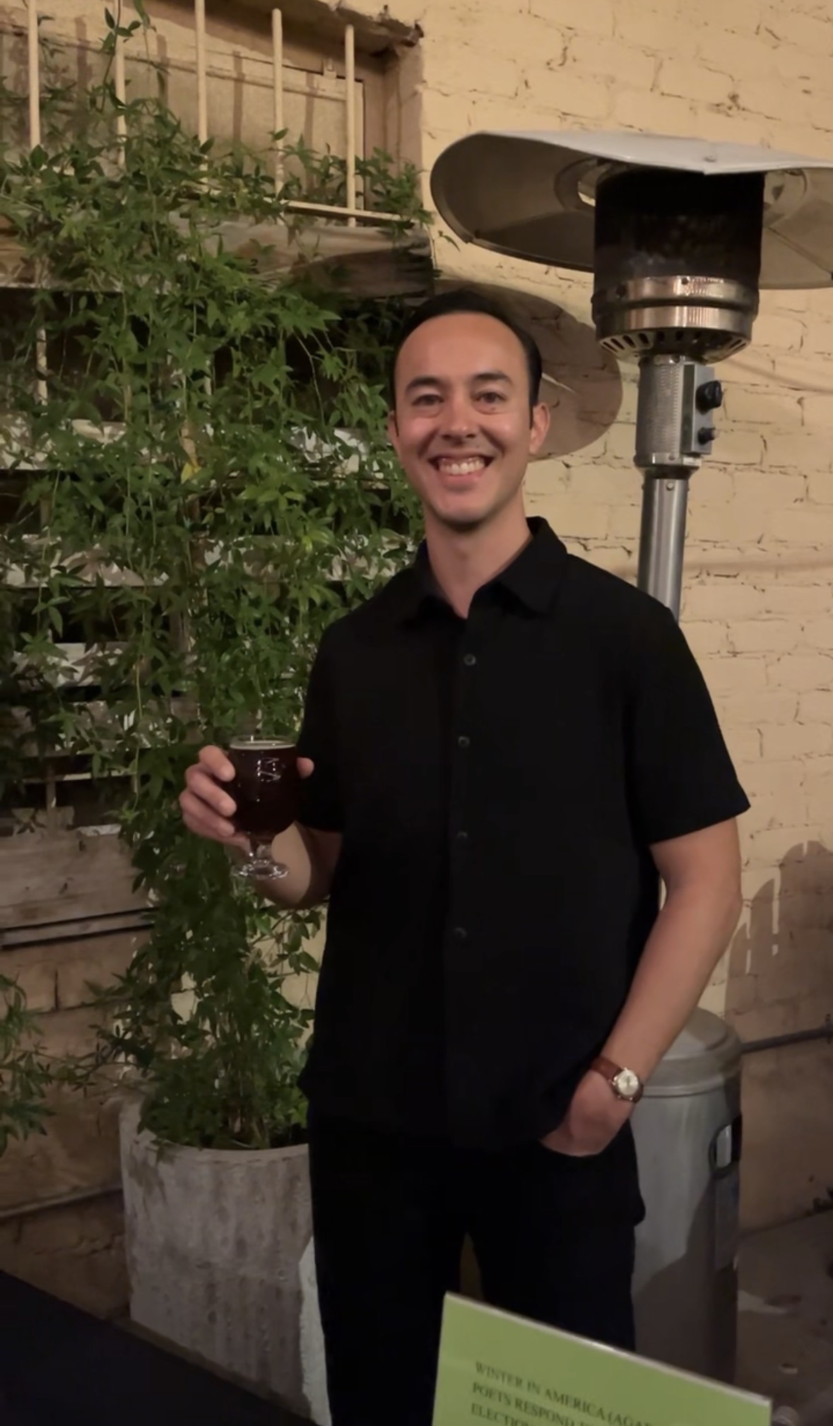 Cameron Quan, an Asian man in his 30s, holds a beer and smiles at the Crested Poetry Reading in Tucson, March 2026