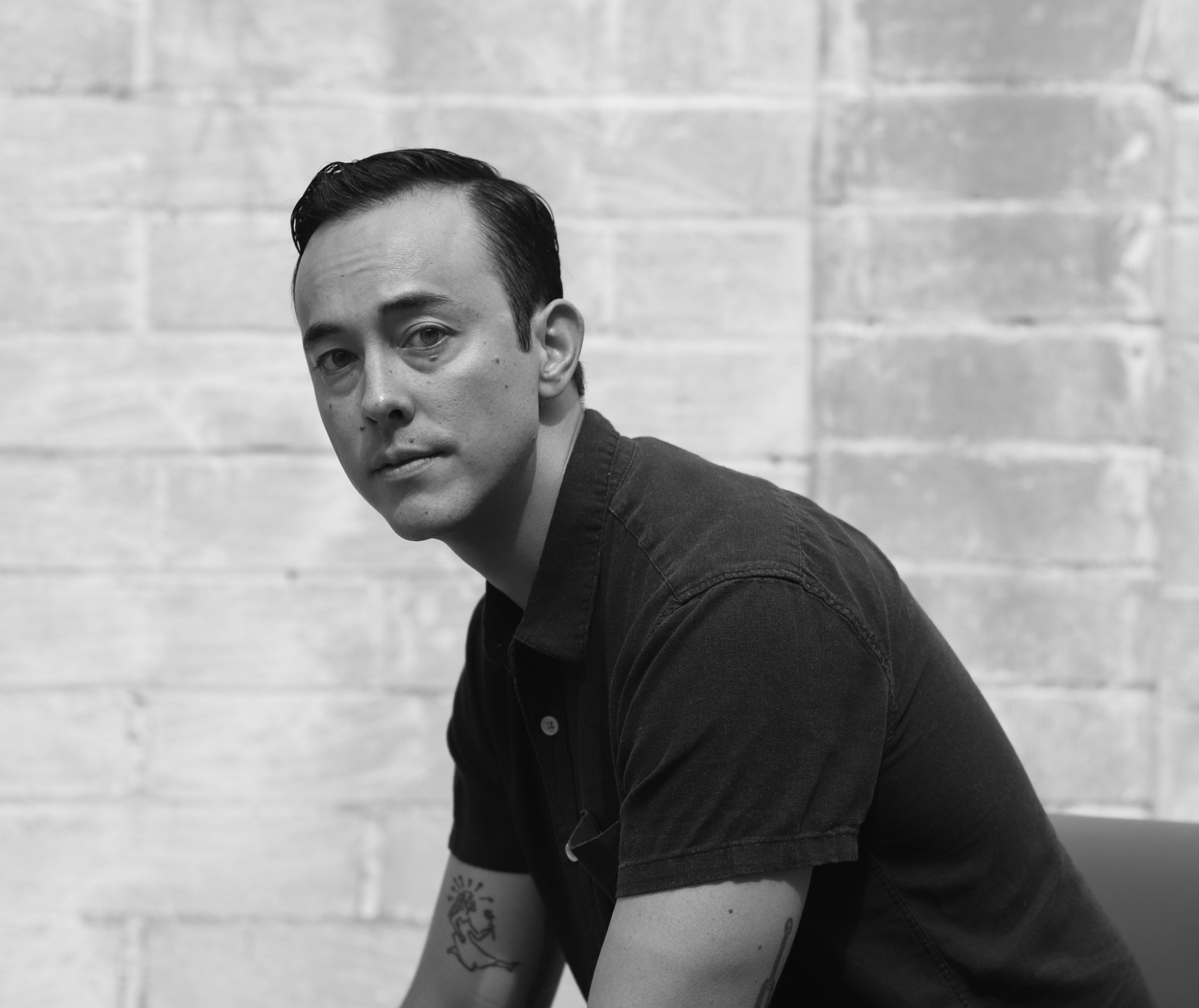 Black and white portrait of an asian american man in his mid-30s against brick wall